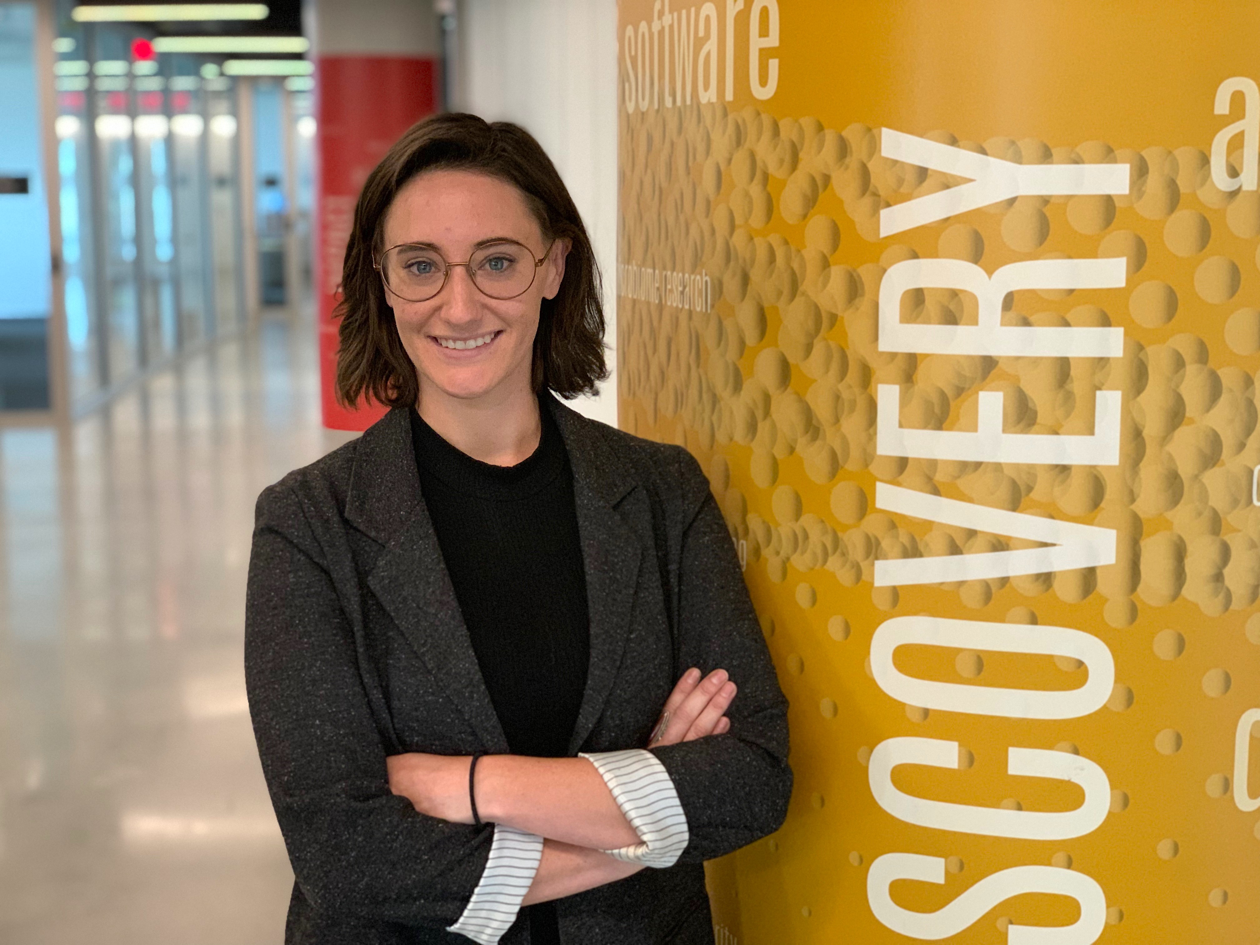 woman in blazer and glasses smiling with arms crossed next to column that says "discovery"