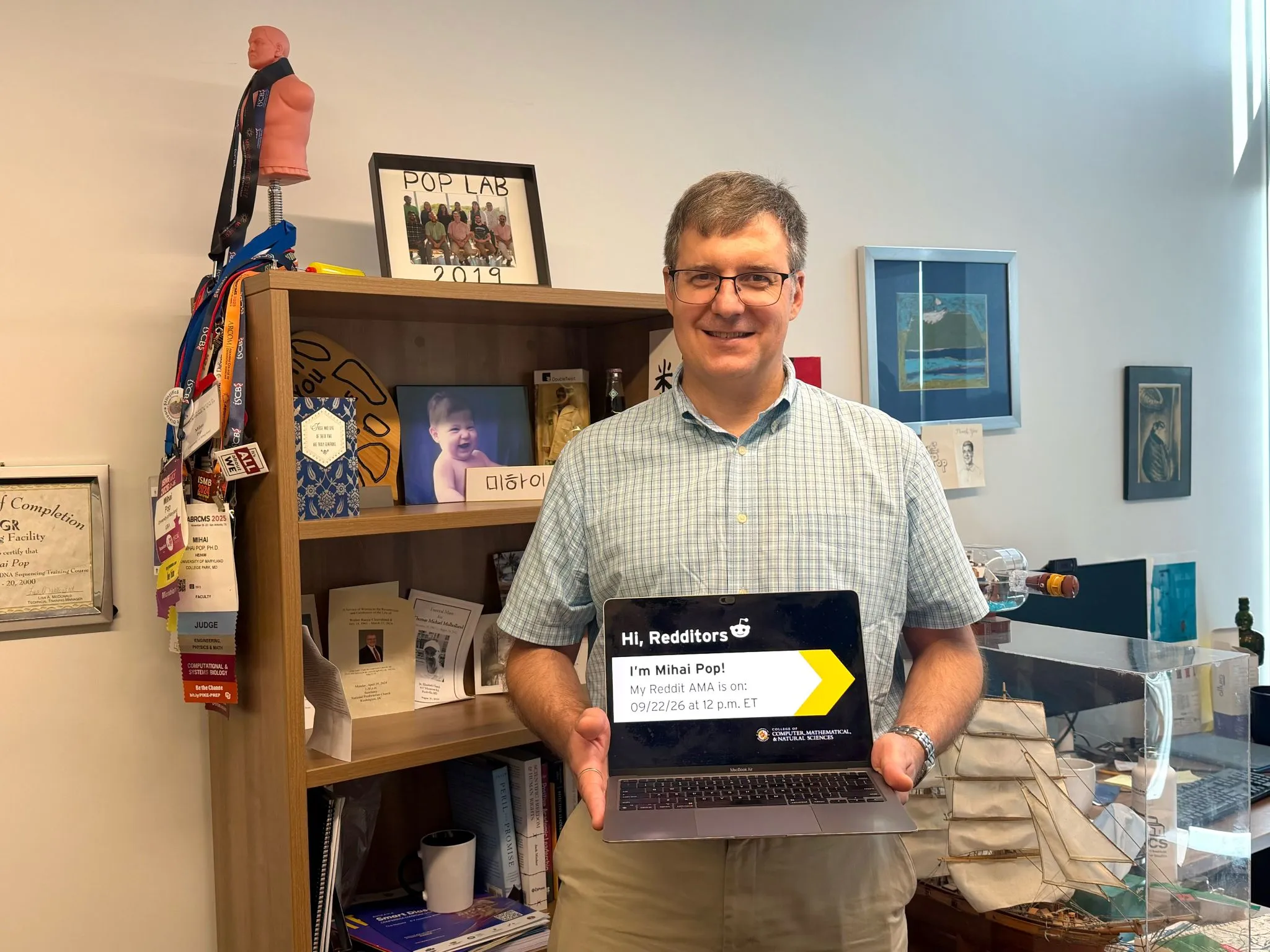 Mihai Pop standing in his office holding an open laptop displaying a Reddit AMA announcement that reads "Hi, Redditors. I'm Mihai Pop!".